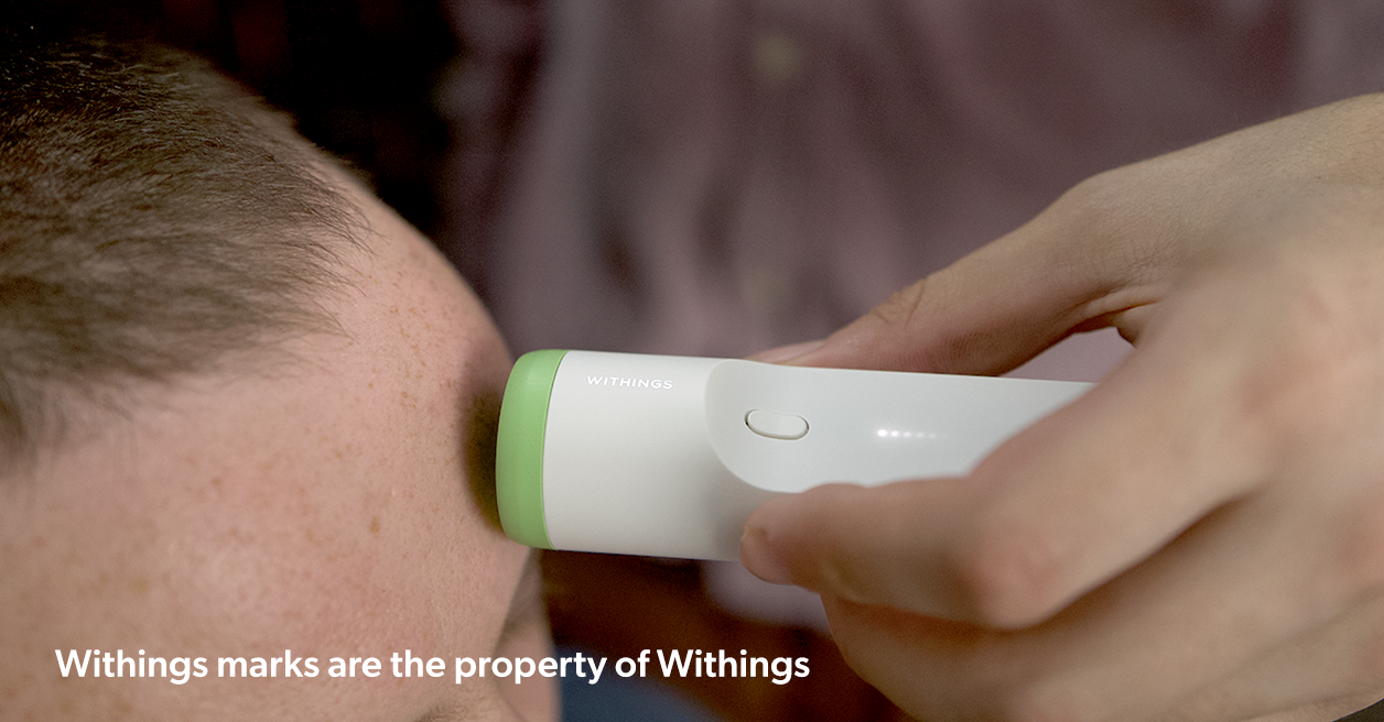 A person measuring the body temperature using a smart withings thermometer